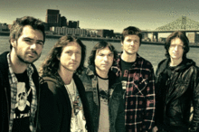 Photo des cinq hommes du groupe de musique : derrière eux un grand pont de Montréal